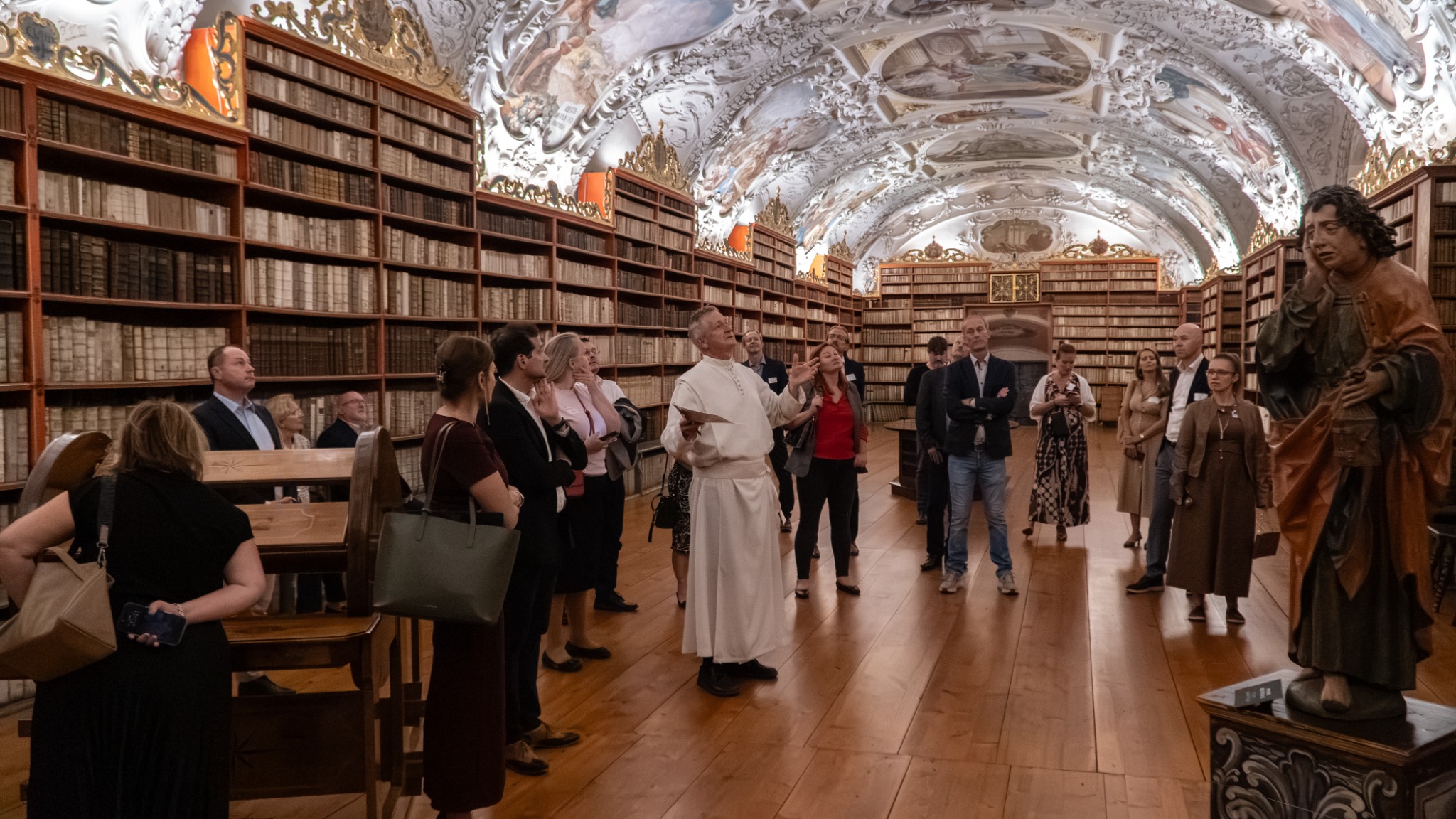 A guide speaking to event guests among historic books and sculptures in the Strahov Library